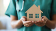 © Fareedoh - Healthcare professional holding house model, symbolizing home care and wellness support in a comforting environment.