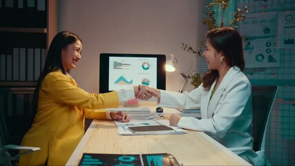 Aufkleber - Two businesswomen are shaking hands after closing a deal in an office at night. They are both smiling and looking happy with the agreement