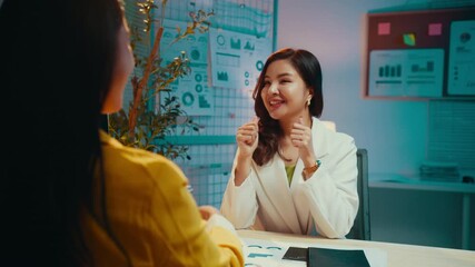 Poster - Two asian businesswomen shake hands in an office, discussing work while smiling. Their interaction reflects teamwork and collaboration in a professional environment
