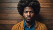 © Nailotl - An adult man with afro hair looks relaxed and serious in front of a light wood wall.