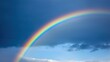 © Danudet.C - Beautiful Rainbow Arching Across a Dramatic Sky with Dark Clouds and Soft Blue Background, Perfect for Nature and Weather Themes in Photography