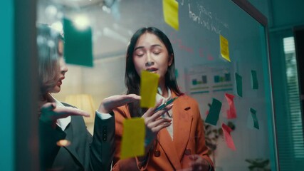 Poster - Two businesswomen engaging in a lively debate while brainstorming ideas, utilizing colorful sticky notes on a glass wall in a modern office setting