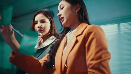 Poster - Two businesswomen brainstorm while using sticky notes on a glass wall in their office, fostering collaboration and generating innovative ideas for their projects