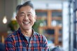 © Markus Schröder - Portrait of a happy asian man in his 50s dressed in a relaxed flannel shirt while standing against modern minimalist interior