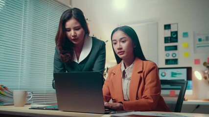 Poster - Two businesswomen work late at night in the office, discussing projects and analyzing data on a laptop. Their collaboration highlights teamwork and dedication in a corporate environment