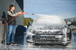 © Serhii - Car wash equipment. A man is washing a car at self service car wash. High pressure vehicle washer machine sprays foam