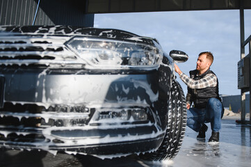 Wall Mural - A man washes a car with a sponge at a self-service car wash