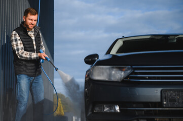 Wall Mural - Car wash. Man washes car with water from high pressure washer