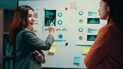 Poster - Businesswoman pointing at a whiteboard filled with charts and graphs, explaining concepts to a colleague during a collaborative office meeting. Engaging discussion fosters teamwork and strategy