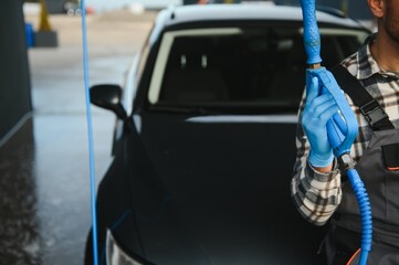 Wall Mural - Man worker in uniform washing standing front car service station. Car wash cleaning station