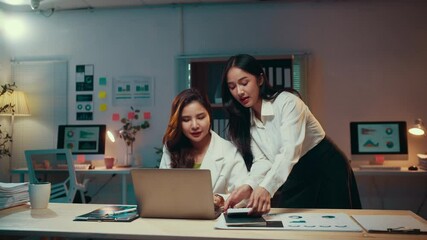 Poster - Two asian businesswomen are working late in their office. They are having a discussion about a project, looking at a laptop screen