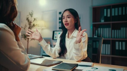 Fototapete - Asian businesswoman is explaining a strategy to her colleague at night. She is gesturing with her hands and speaking in a clear voice