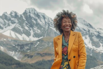 Wall Mural - Portrait of a cheerful afro-american woman in her 60s dressed in a stylish blazer on backdrop of mountain peaks