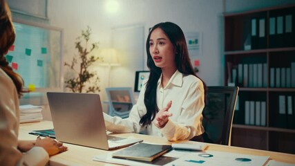 Poster - Young asian businesswoman leads a meeting with her colleague in a late-night office setting. Engaging in discussions, they focus on strategy and collaboration while reviewing data and charts
