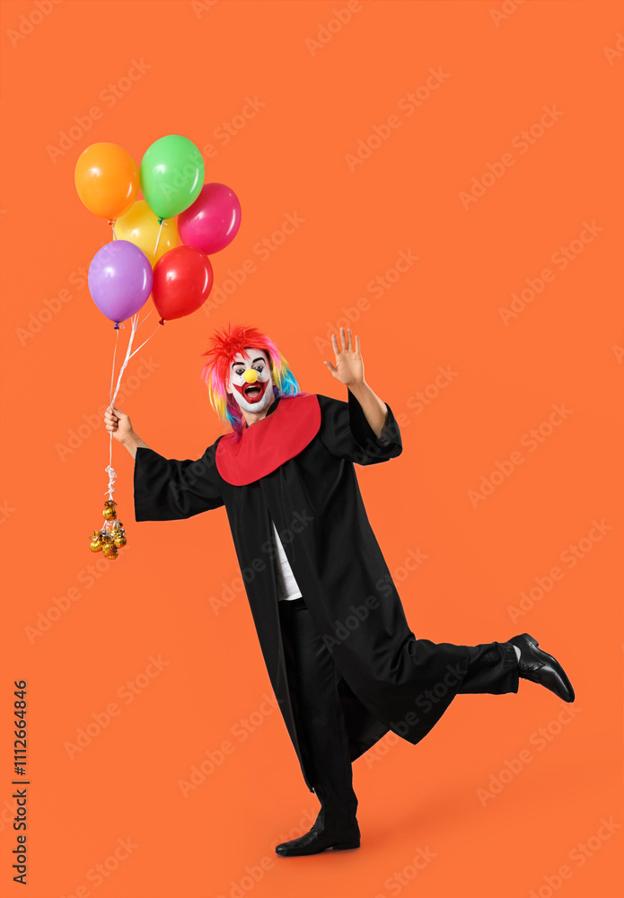 Surprised graduating student dressed as clown with balloons waving hand on orange background