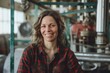 © Markus Schröder - Portrait of a grinning woman in her 40s dressed in a relaxed flannel shirt in bustling factory floor
