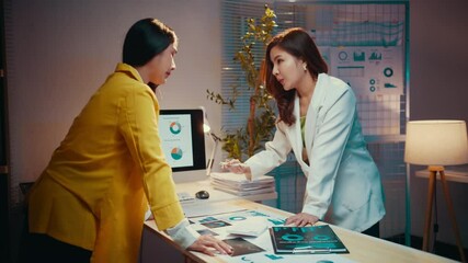 Poster - Two businesswomen are having an animated discussion about paperwork in the office at night. They are leaning over a desk and gesturing with their hands