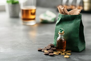 Wall Mural - Green money bag with scattered coins and glass bottle of whiskey on gray concrete background. Financial savings concept. Banking and wealth. Side view with copy space