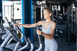 © ty - Attractive cheerful sportswoman in grey t-shirt exercising actively on elliptical trainer