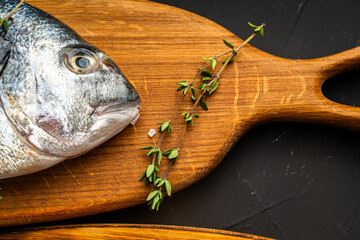 Wall Mural - Fish dorado on a wooden board and oregano on a black background. Close-up. Top view