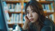© MUHAMMADALAN - Young woman thoughtfully looking at computer screen in library.