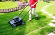 © jamal - Man trimming overgrown green lawn with electric mower in garden, gardener using lawn trimmer, while landscaping