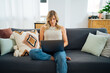 © Manu Padilla/Stocksy - Woman sitting on couch using laptop in living room