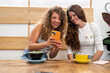 © Alvaro Lavin/Stocksy - Two friends laughing at a smartphone while sitting at a coffee shop