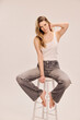© MACO - Portrait of young beautiful woman sitting on a stool in a studio setting.