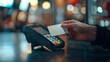 © HA - A hand holds a credit card near a POS terminal for a contactless payment. The scene is set at night with a blurred background of lights.