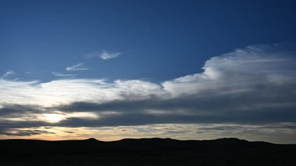 Wall Mural - time lapse of late day clouds in blue sky above a hilly silhouette setting