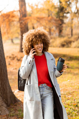 Enjoying a sunny autumn day while chatting on the phone and sipping a warm drink in the park