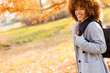 © BGStock72 - Young woman with curly hair smiles warmly while exploring a vibrant autumn park in sunny daylight