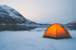 © jr-art - A small orange tent is set up in the snow next to a lake