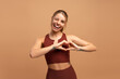 © Maria Vitkovska - Happy young sporty woman showing heart shape with hands, winking in studio