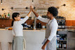 © BONNINSTUDIO/Stocksy - Two young cafe workers giving high five at coffee shop