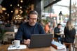 © Milos - A focused man works on his laptop in a modern café while enjoying a cup of coffee, representing the blend of productivity and leisure in a contemporary urban lifestyle.