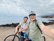 © Daniel - Two happy old mature people enjoying and riding bikes together to be fit and healthy outdoors. Active seniors having fun taking a selfie picture with camera