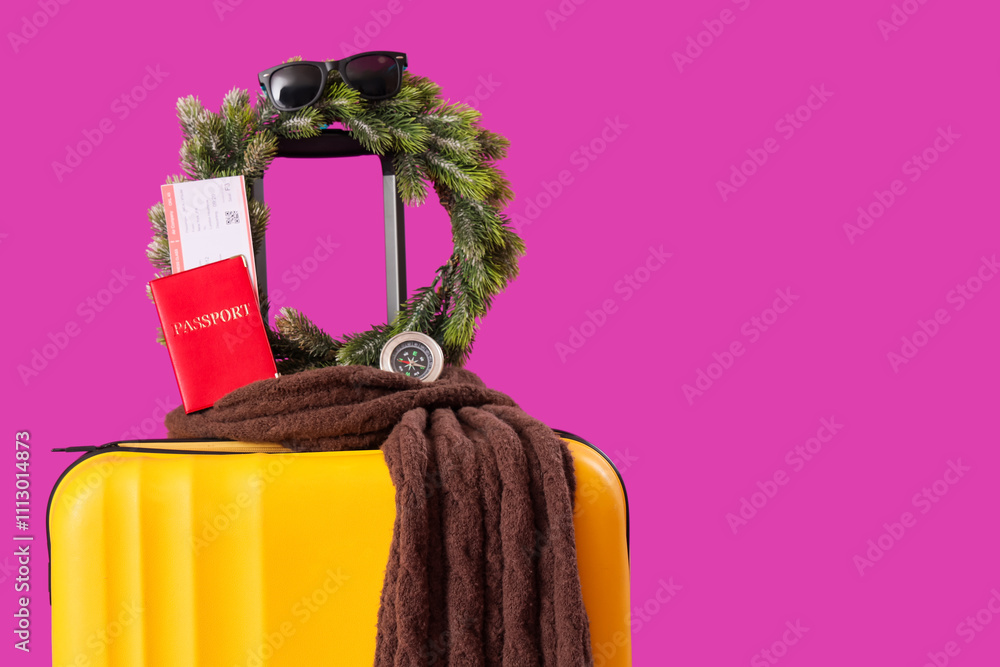 Suitcase with Christmas accessories and passport on purple background