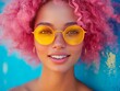 © Mister - A vibrant, pink-haired individual is shown with a bright smile and yellow sunglasses in a blue gradient background The image exudes fashionable energy for an advertisement or editorial feature