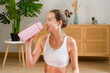 © mahalo studio/Stocksy - sporty woman drinking water from pink bottle at home