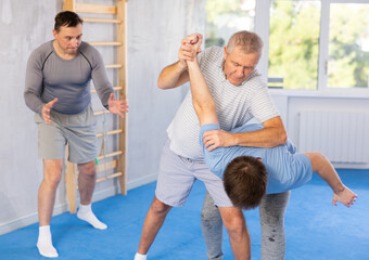 Wall Mural - Elderly man and young man training self-defense techniques in studio..