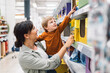© Santi Nuñez/Stocksy - Mother helping her son reach for a product on a grocery store shelf