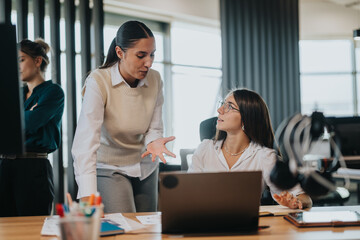 Wall Mural - Two business people engaged in a conversation at a desk, demonstrating teamwork and communication in a contemporary workplace environment.