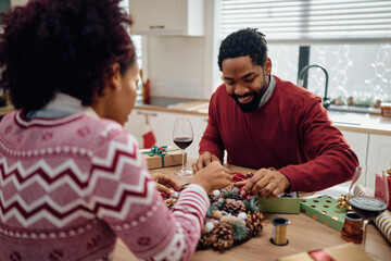 Wall Mural - Happy black man and his wife enjoying in making Christmas wreath while decorating their home for holidays.