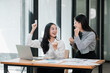 © Satori Studio - Two joyful businesswomen celebrate a successful project in a modern office, surrounded by laptops and documents.
