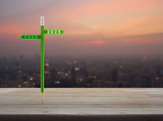 Canvas Print - 2025 and 2024 direction sign plate with green pencil on wooden table over blur of cityscape on warm light sundown, Business happy new year strategy and planning concept