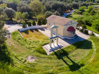 An aerial view of a quaint, yellow rural church in Kopsochilades village  with a tiled roof, nestled amidst greenery. The serene setting and simple architecture evoke a sense of peace and tranquility.