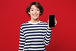 © ViDi Studio - Young surprised shocked happy woman wear blue striped sweatshirt casual clothes hold in hand use mobile cell phone with blank screen workspace area isolated on plain red background. Lifestyle concept.