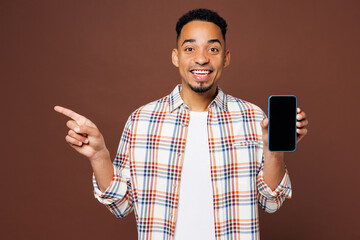 Canvas Print - Young man of African American ethnicity in blue shirt casual clothes hold in hand use mobile cell phone with blank screen area point finger aside isolated on plain brown background Lifestyle concept